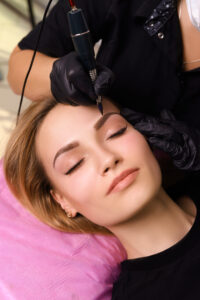 Cosmetologist applying permanent make up on eyebrows- eyebrow tattoo.