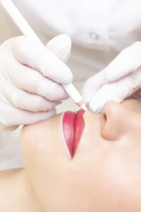 Young woman having permanent makeup on her lips at the beauticians salon. Permanent Makeup (Tattoo). drawing a contour with a white lip pencil. vertical photo